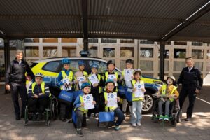 Kinder mit Beeinträchtigung stehen mit einer Urkunde zusammen mit zwei Polizistinnen vor einem Polizeiauto Kinder mit Beeinträchtigung stehen mit einer Urkunde zusammen mit zwei Polizistinnen vor einem Polizeiauto